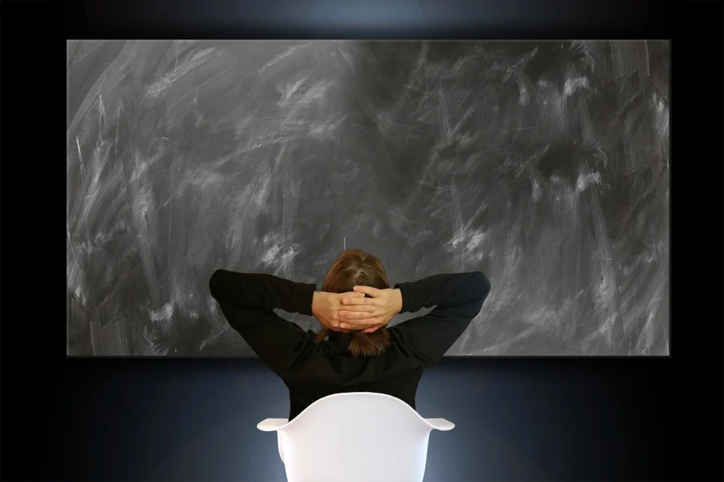 A woman seated and staring at a blank blackboard