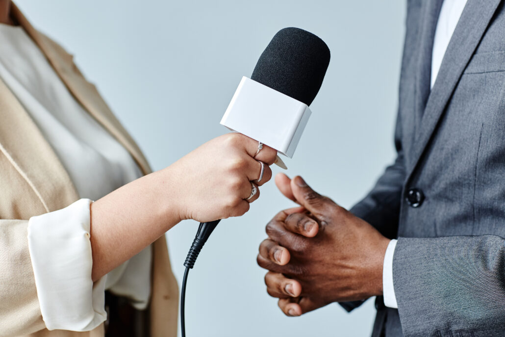 Side view closeup of young woman journalist holding microphone while interviewing business expert