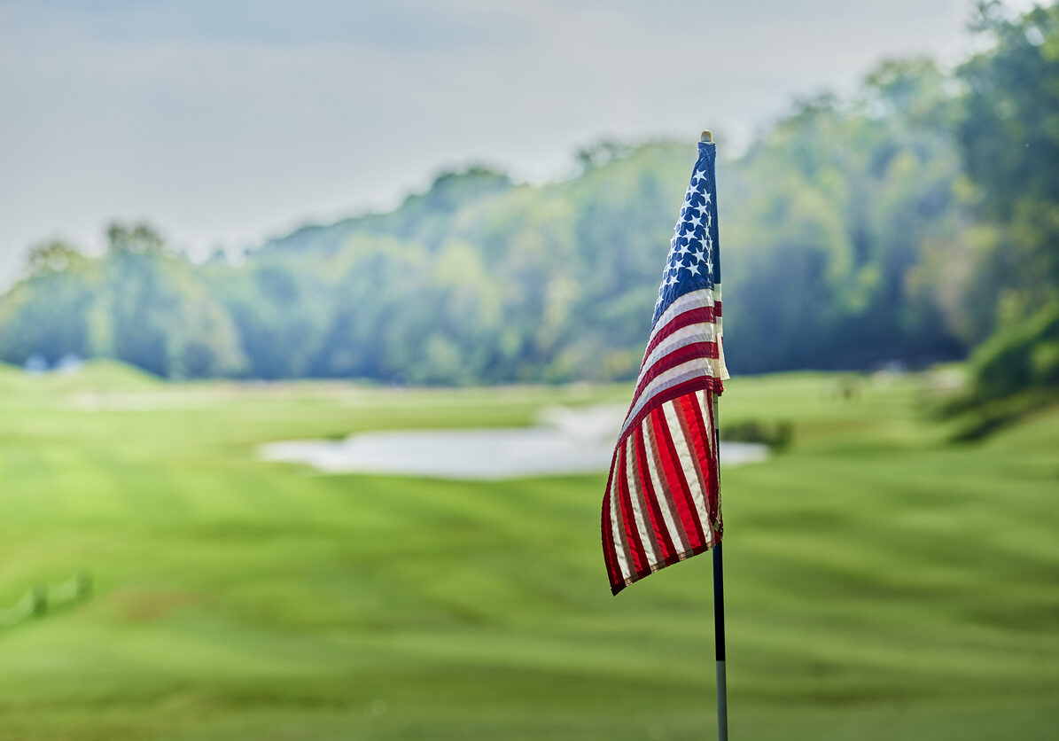 An American flag in the foreground before a background of an emerald green golf course